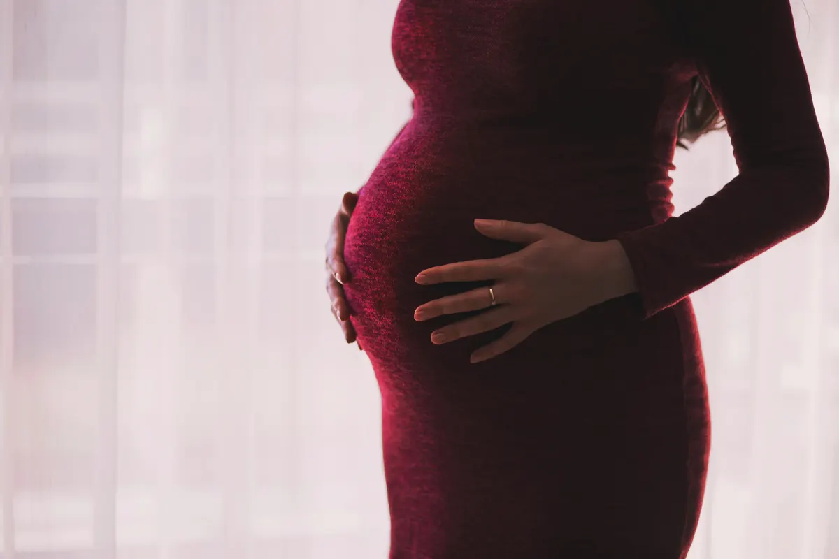 Pregnant woman in a red dress with one hand on her bump and one on her lower back
