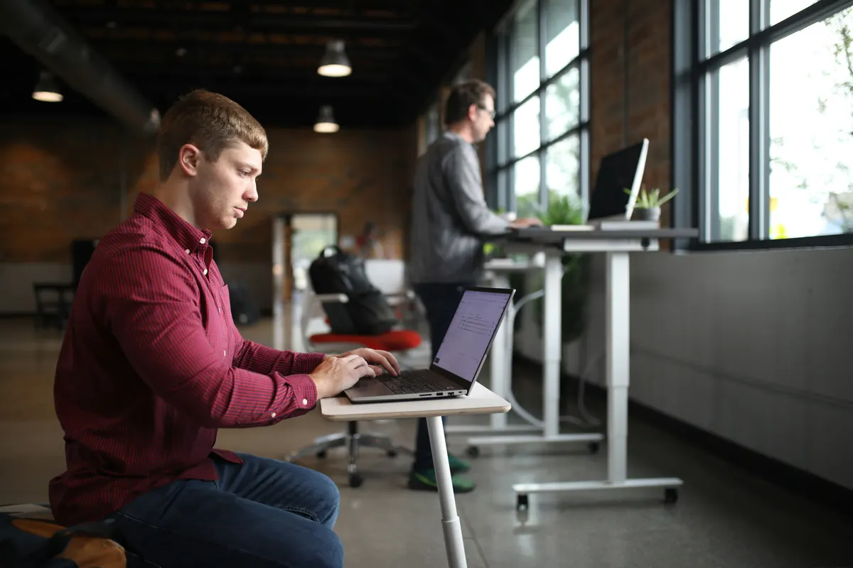 Young man hunched over a laptop at a low desk in an office