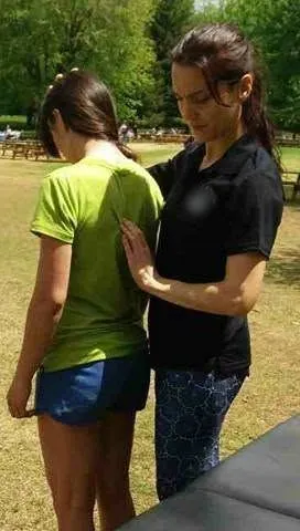 Osteopath assessing a patient's upper back, outdoors in a park