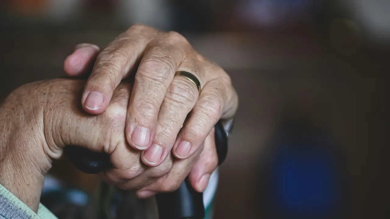 Older person's hands resting on the handle of a walking cane