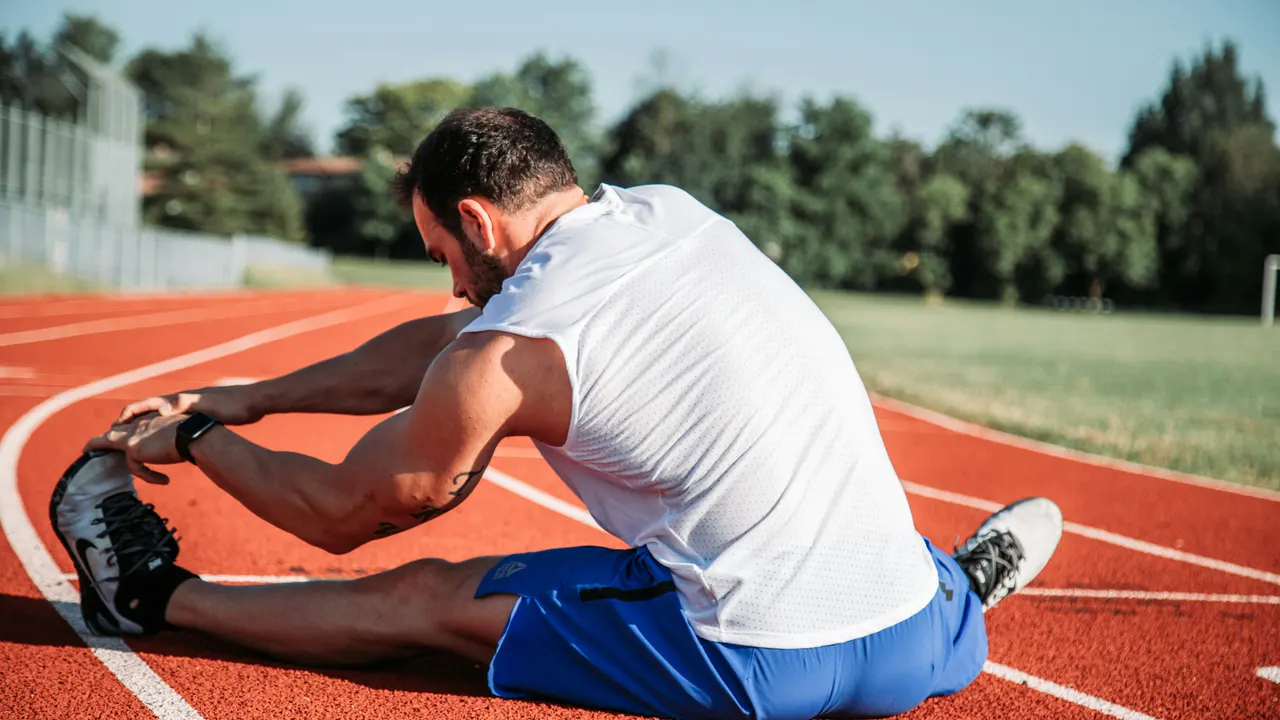 Runner sitting on an athletics track, stretching his hamstrings
