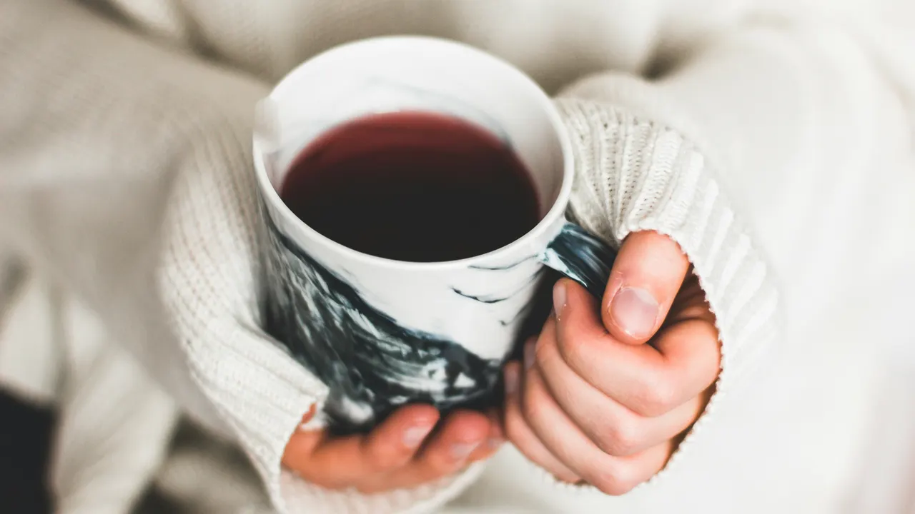 Hands in a knitted sweater holding a cup of tea